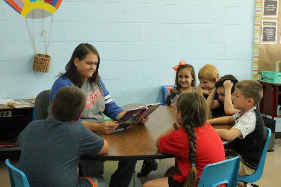 Mrs. Booth sits in class reading to her third grade students. 